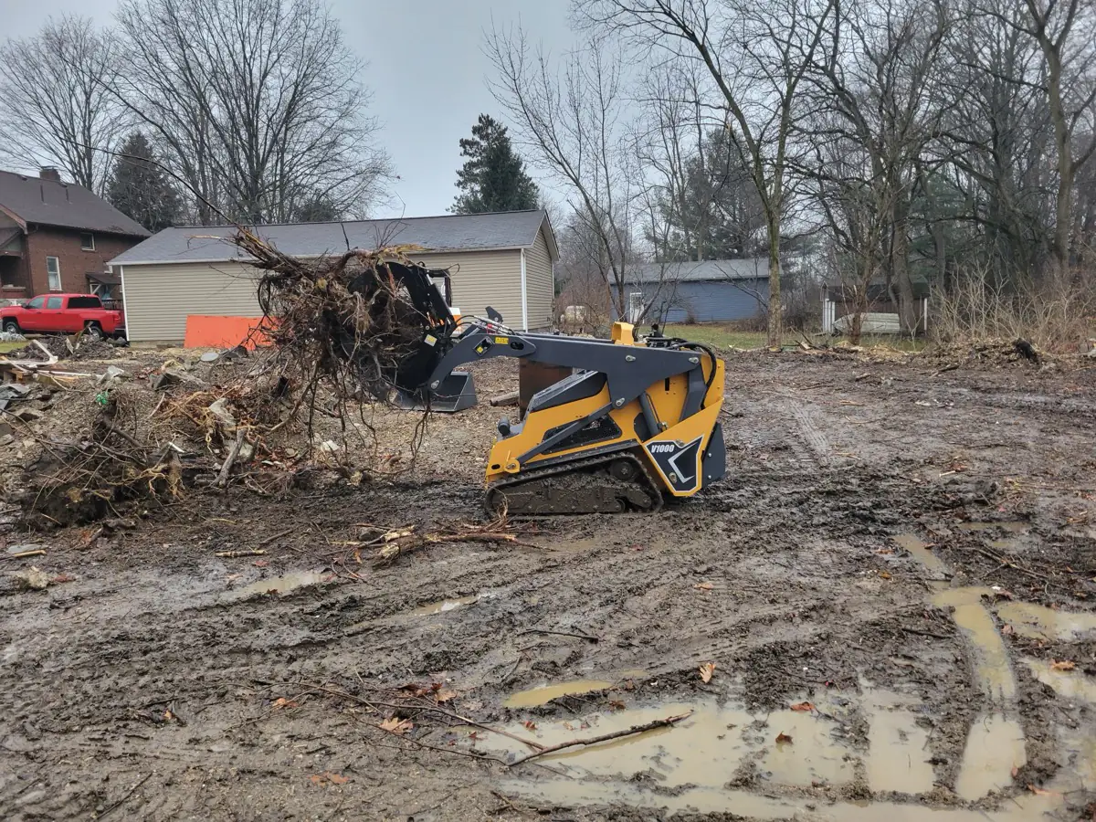 Track loader hauling a root ball away during lot clearing in a neighborhood